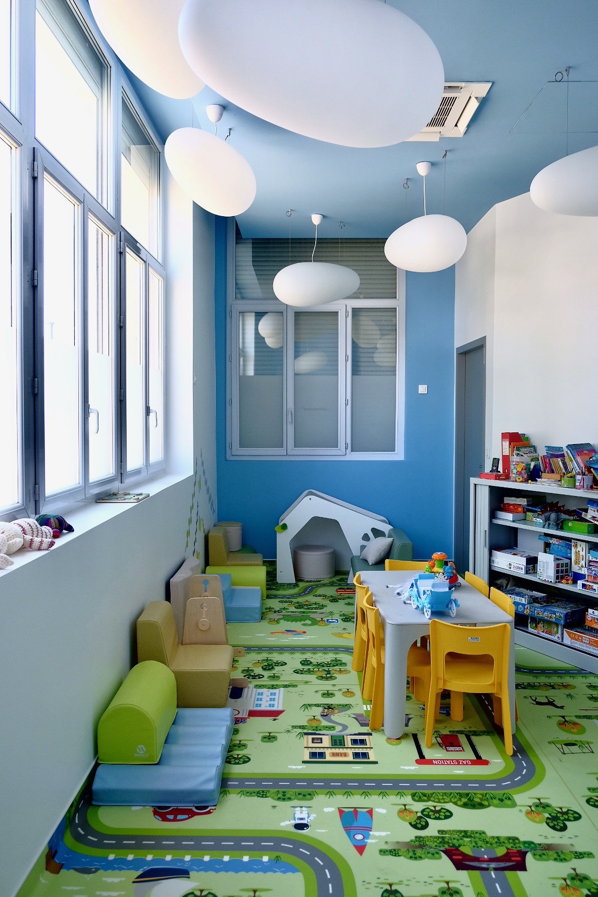 Pièce d'accueil des enfants avec petites table et chaises, bibliothèques, armoire avec jouets et jeux